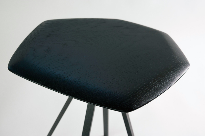 tabouret bas, assise en chêne teinté noir en forme de polygone irrégulier. piétement évasé formé de quatre barres fines d'acier noir sablé 